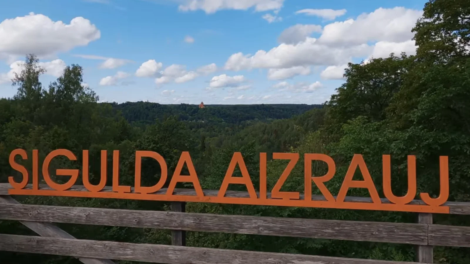 Orange Sigulda sign overlooking the forested Gauja Valley under a blue sky